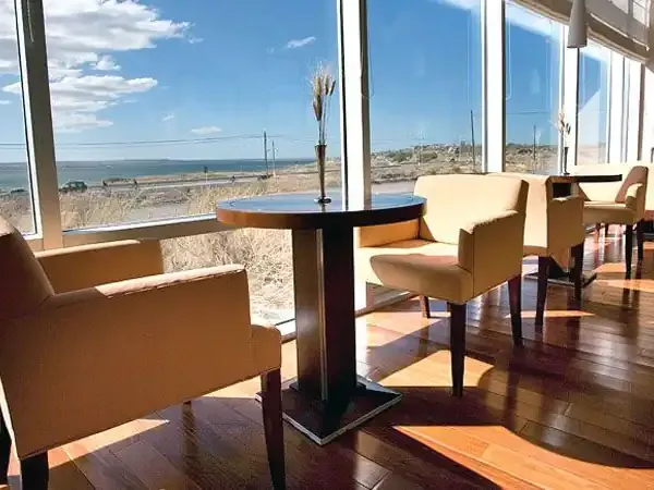 Modern lounge with floor-to-ceiling windows overlooking Patagonian coastal landscape and steppe terrain.