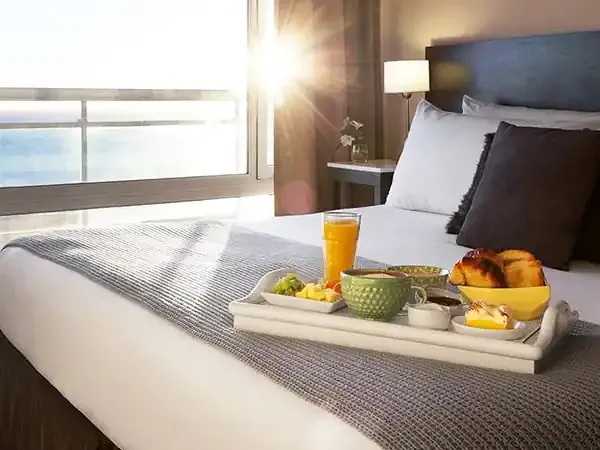 Luxury hotel bedroom with ocean view, breakfast tray, and morning sunlight in Puerto Madryn.