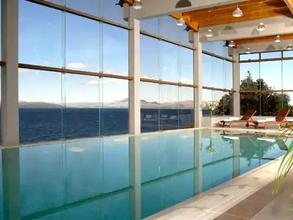 Luxury indoor pool with floor-to-ceiling windows overlooking Patagonian lake and mountains at Alma del Lago resort.