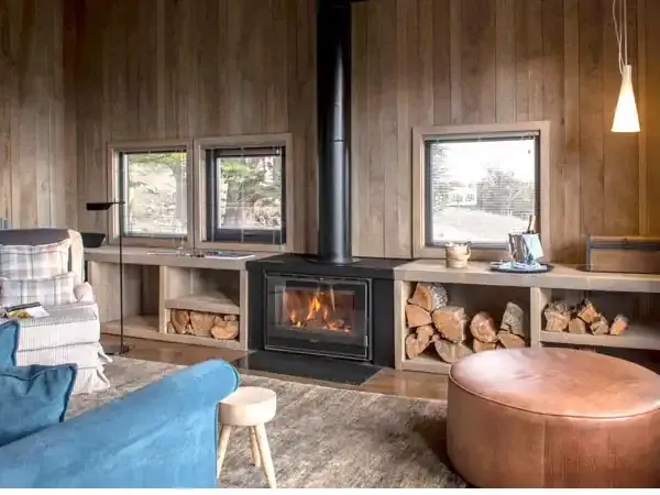 Modern lodge interior with wood-paneled walls, fireplace, leather furnishings, and panoramic windows overlooking Patagonian landscape.