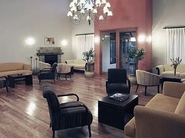 Elegant hotel lobby in Elena featuring beige and black mid-century modern furniture, polished wood floors, and ambient lighting.
