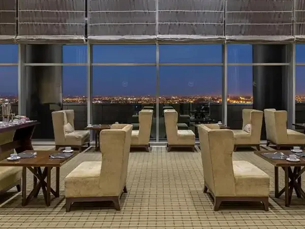 Luxury lounge at Sheraton Mendoza with panoramic city lights views, cream armchairs, and fine dining setup at dusk.