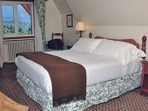 Elegant bedroom at Llao Llao hotel with mountain views, white bedding, and traditional Patagonian décor overlooking the Andes.