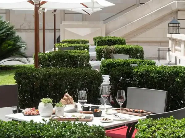 Elegant outdoor dining setup at Park Hyatt with white table, wine glasses, and manicured green hedges under umbrellas.