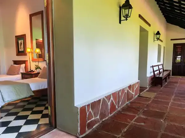 Colonial-style hotel corridor with terra cotta tiles, dark wood doors, and a bedroom view featuring checkered flooring at Rincón del Socorro.