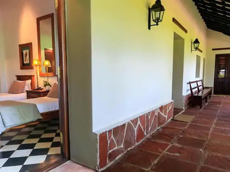 Colonial-style hotel corridor with terra cotta tiles, dark wood doors, and a bedroom view featuring checkered flooring at Rincón del Socorro.
