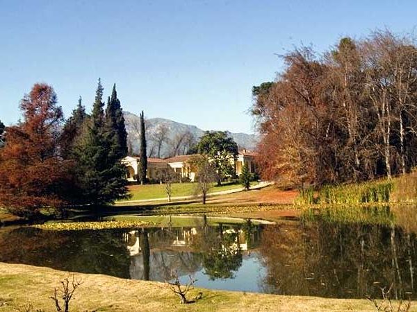 Serene lake at Viña Concha y Toro in Santiago de Chile, with autumn trees, manicured gardens, and a historic mansion reflected in still water.