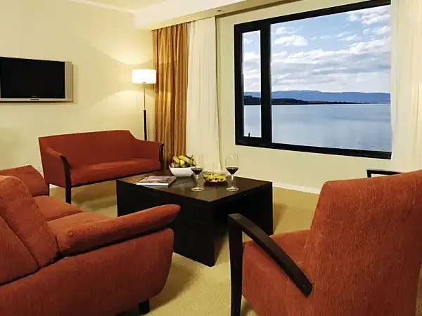 Luxury hotel suite with red armchairs, lake view through large windows, and modern amenities overlooking Patagonian waters.