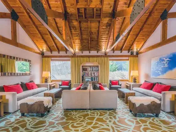 Luxury lodge living room at Mirador del Lago with exposed wooden beams, floor-to-ceiling windows overlooking Patagonian mountains, and contemporary furnishings.