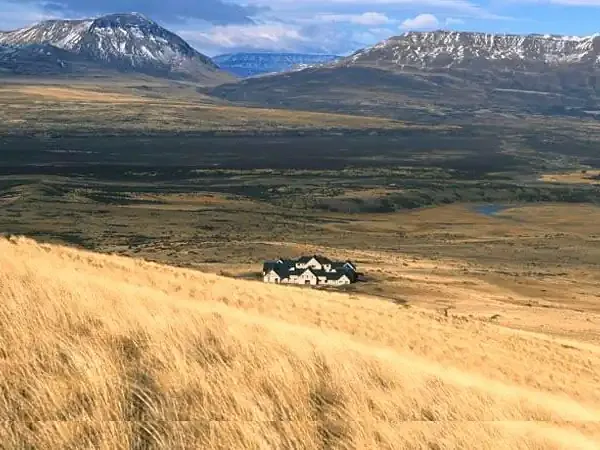 Sprawling Patagonian valley with snow-capped mountains, golden grasslands, and a remote estancia nestled in the vast landscape of El Chaltén region.