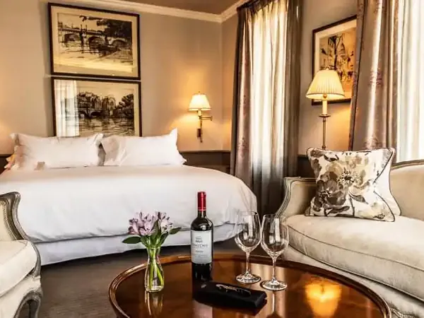 Luxurious Santiago hotel suite featuring a pristine bed, elegant seating area, wine service, and warm ambient lighting.
