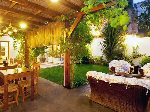 Cozy outdoor patio at Ecohotel Carmenere with dining tables, wicker seating, lush gardens, and warm ambient lighting.