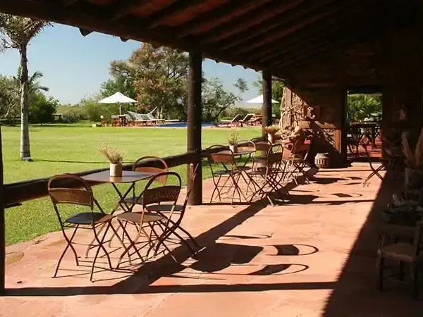 Covered patio with dining tables overlooking expansive grounds at Aguapé Lodge, a rural Patagonia estancia with manicured lawns and distant countryside.