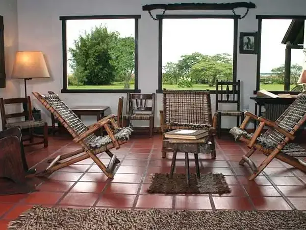 Rustic lodge interior with leather recliners overlooking green Patagonian landscapes through large windows.