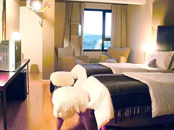 Luxury hotel room with twin beds, mountain views through floor-to-ceiling windows, and modern Patagonia alpine resort ambiance.