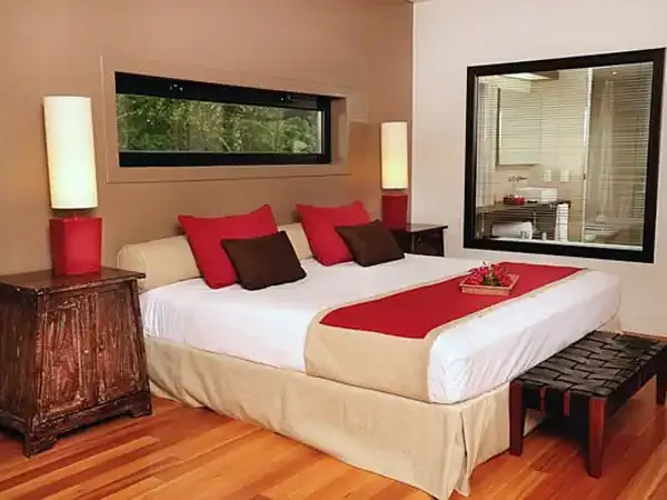 Modern luxury bedroom at Fierro Hotel Buenos Aires with red accents, wooden floors, and panoramic windows overlooking the garden.