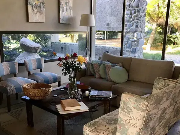 Elegant living room at Finca La Azul with stone views, striped armchairs, and floor-to-ceiling windows overlooking Patagonian gardens.