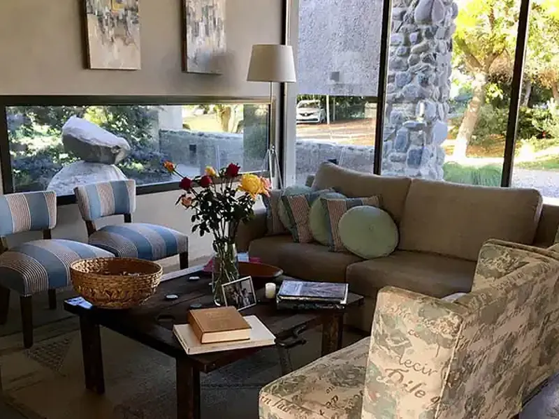 Elegant living room at Finca La Azul with stone views, striped armchairs, and floor-to-ceiling windows overlooking Patagonian gardens.