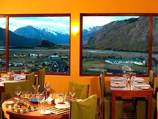 Upscale dining room with panoramic windows overlooking snow-capped mountains and a valley settlement in Patagonia.