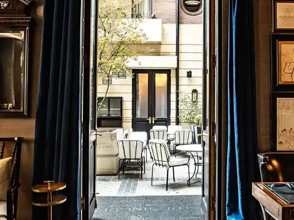 Elegant Santiago hotel room with dark wood interiors, gold accents, and open doors revealing a modern courtyard patio with contemporary seating.