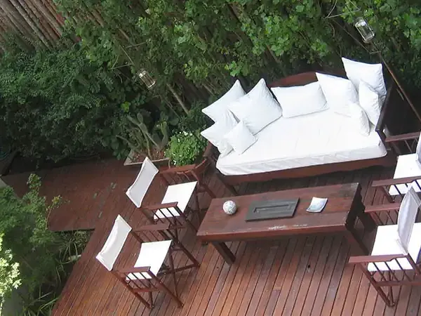Overhead view of a luxurious wooden deck with white bedding, potted plants, and director's chairs overlooking lush greenery.