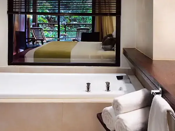 Luxury spa bathroom at Fierro Buenos Aires hotel with whirlpool tub, rolled towels, and bedroom view.