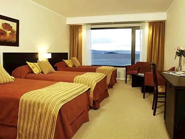 Luxury hotel room with multiple beds, warm furnishings, and panoramic lake views in Patagonia.