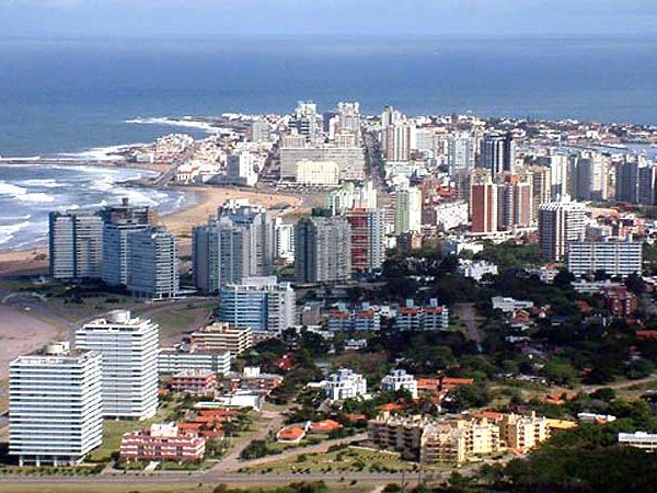 Aerial view of Puerto Madryn's beachfront cityscape with high-rise hotels and residential buildings along the Atlantic coast.
