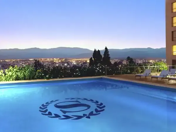 Rooftop pool at Sheraton hotel overlooking illuminated city and mountains at twilight in Buenos Aires.