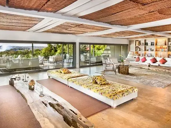 Luxurious modern living room at Gran Meliá Iguazú with natural wood ceiling, floor-to-ceiling windows overlooking lush landscapes, and contemporary furnishings.