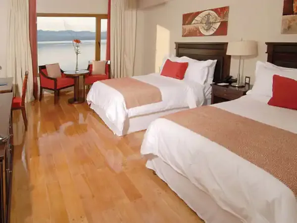 Luxury lakeside hotel room at Alma del Lago with two queen beds, red accents, and panoramic lake views through floor-to-ceiling windows.