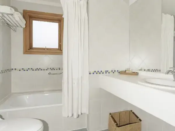 Modern white bathroom with decorative tile accents, double vanity, and bathtub at Hotel Las Torres.