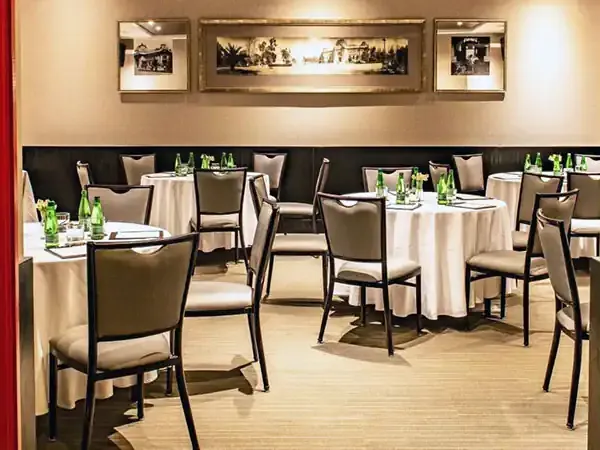 Elegant dining room in Santiago with round tables, cream linens, black chairs, and framed historical photographs.