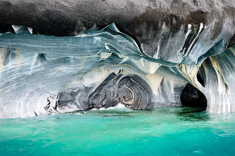 Turquoise waters lap against white and gray marble caves carved into towering cliffs at Capillas de Mármol in Patagonia.