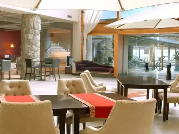 Luxury hotel lobby at Incayal with cream upholstered chairs, dark wood tables, stone columns, and panoramic windows overlooking Patagonian landscapes.