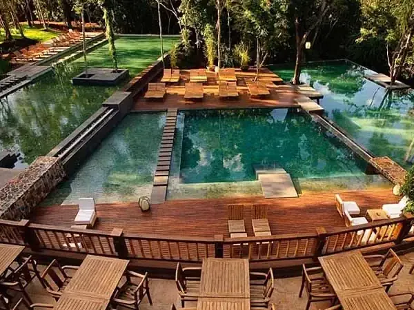 Wooden deck and loungers overlook a crystal-clear natural pool surrounded by lush trees at a luxury Patagonian lodge retreat.