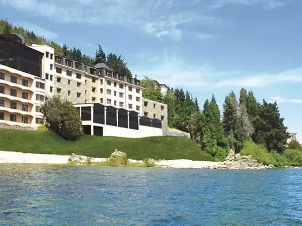 Modern lakeside resort nestled among forests with mountains in the distance along a pristine alpine lake.