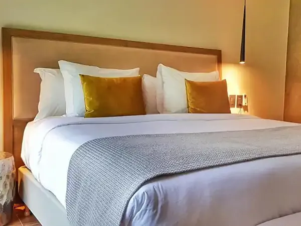 Luxurious hotel bedroom at Selvaje Lodge featuring a king bed with gold velvet pillows, crisp white linens, and warm ambient lighting.
