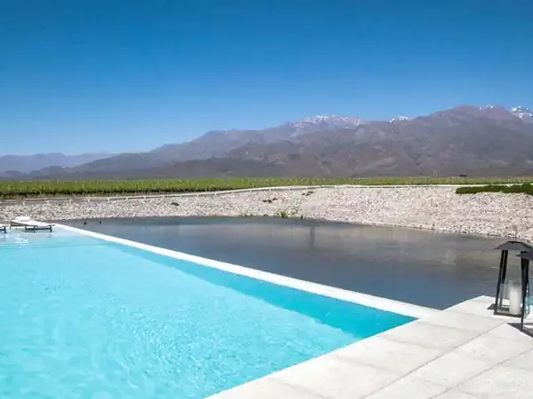 Luxury infinity pool overlooking a river and vineyards with snow-capped Andes mountains in Casa de Uco, Mendoza.