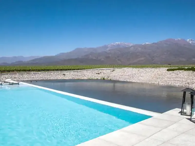 Luxury infinity pool overlooking a river and vineyards with snow-capped Andes mountains in Casa de Uco, Mendoza.