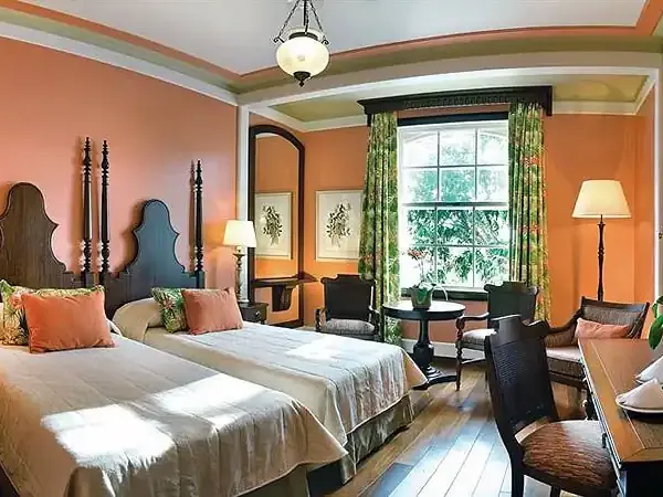 Luxurious bedroom suite at Belmond hotel with twin beds, orange walls, green curtains, and elegant dark wood furnishings.