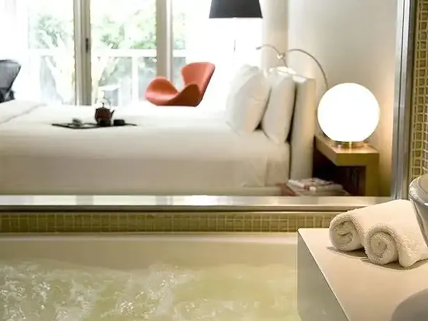 Luxury hotel bathroom in Buenos Aires with soaking tub overlooking modern bedroom with red accent chair.
