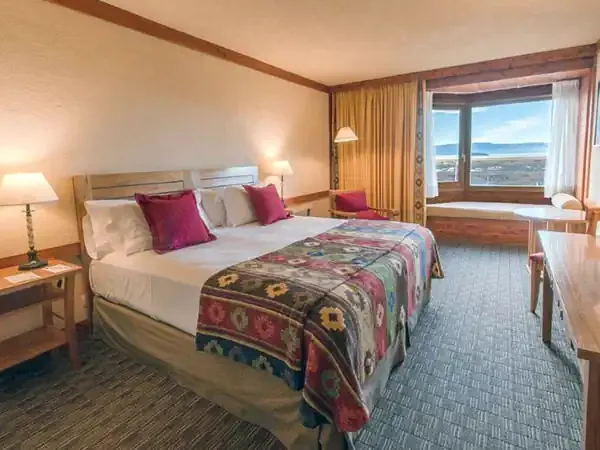 Luxury hotel bedroom with panoramic lake views at Mirador del Lago, featuring modern wood furnishings and warm lighting.