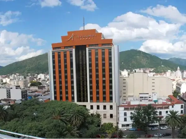 Modern orange and white Alejandro hotel building overlooking a valley city nestled among green mountains under blue sky.