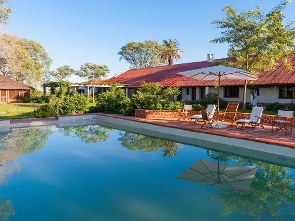 Luxury estancia in Rincón del Socorro features a sparkling blue pool with loungers, red-roofed buildings, and lush gardens.