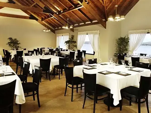 Elegant dining room with round tables, black chairs, white tablecloths, and exposed wooden beams overlooking Patagonian landscapes.