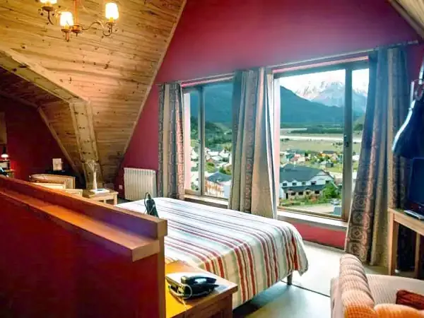 Luxurious bedroom with burgundy walls, wooden beams, and panoramic mountain valley views at Los Cerros Boutique Hotel.