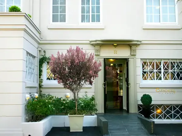 Elegant facade of Carmenere Ecohotel in Buenos Aires with cream-colored walls, manicured gardens, and architectural details.