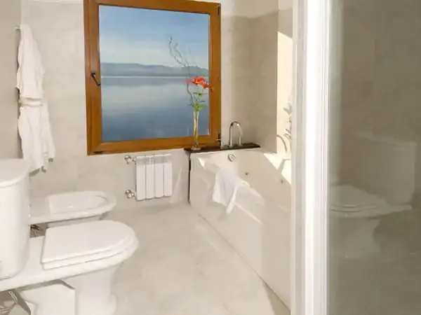 Luxury bathroom with lake view window overlooking Patagonian landscape at Alma del Lago resort.