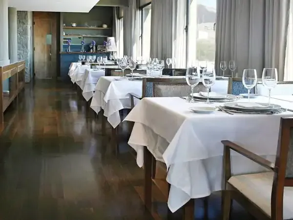 Elegant fine dining restaurant with white tablecloths, formal place settings, and panoramic windows overlooking Patagonian landscapes.